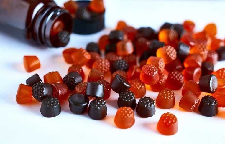 bé gái đang vui vẻ cầm và ăn kẹo dẻo bổ sung vitamin